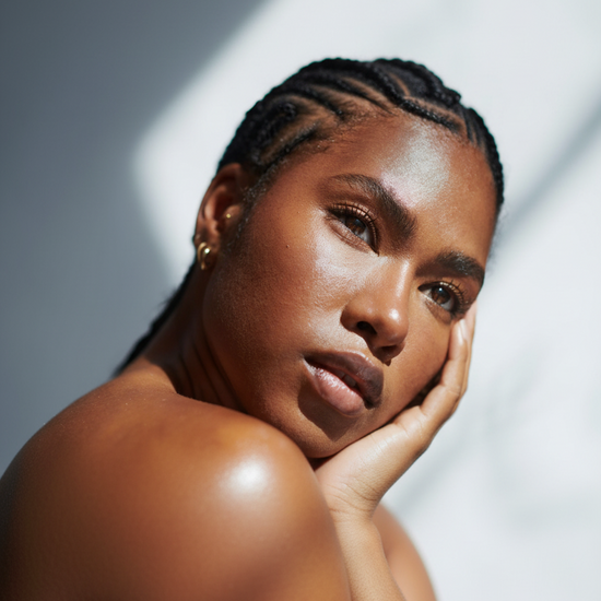 A close-up portrait of a woman with braided hair resting her head on her hand, set against a gray background with dramatic diagonal light beams.