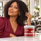 Coconut oil defining curl jelly jar next to curly-haired model in a maroon top